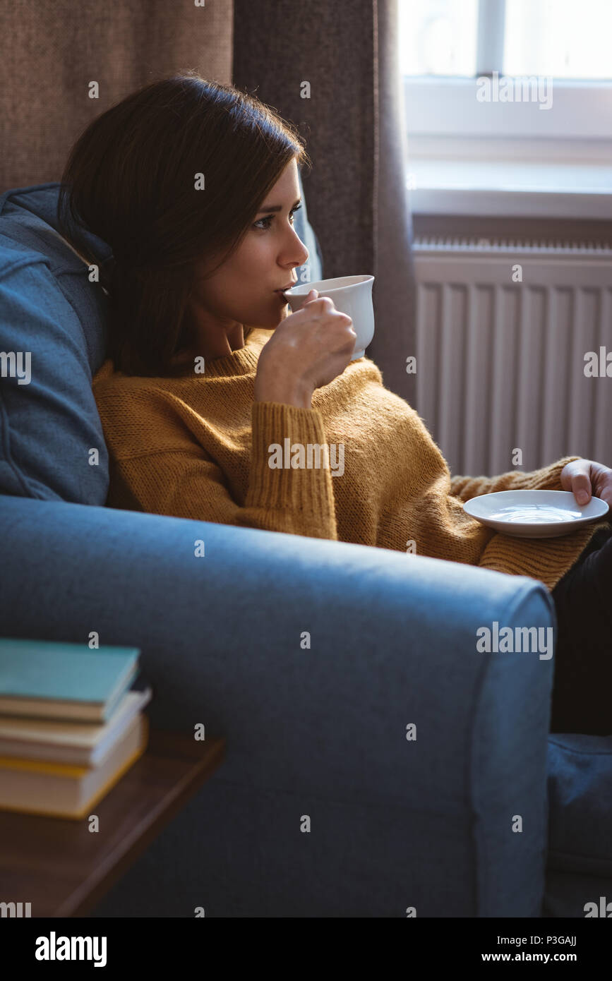 Young woman relaxing on sofa having a coffee during daytime at home Stock Photo