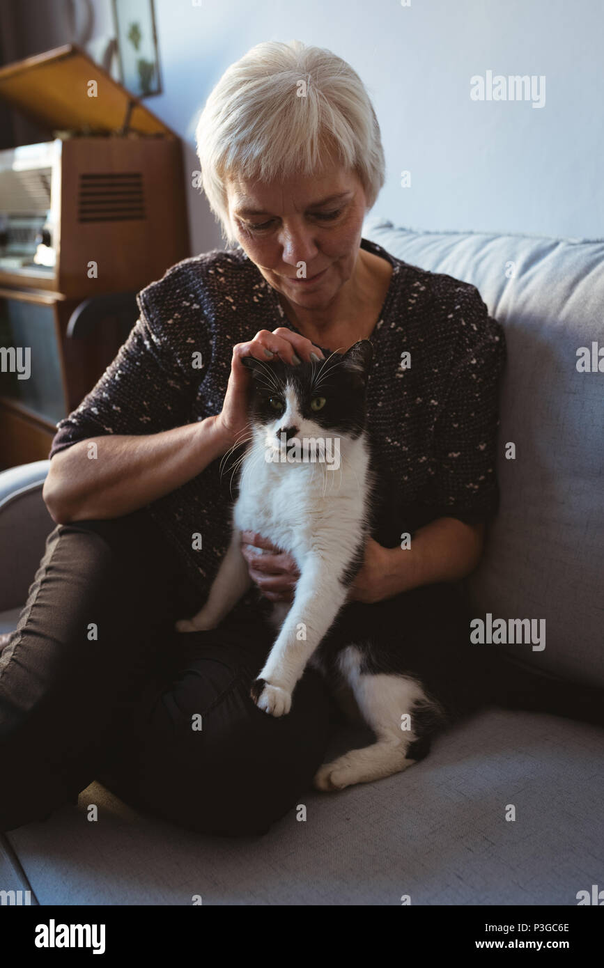 Senior woman sitting on sofa stroking her pet cat in living room Stock Photo