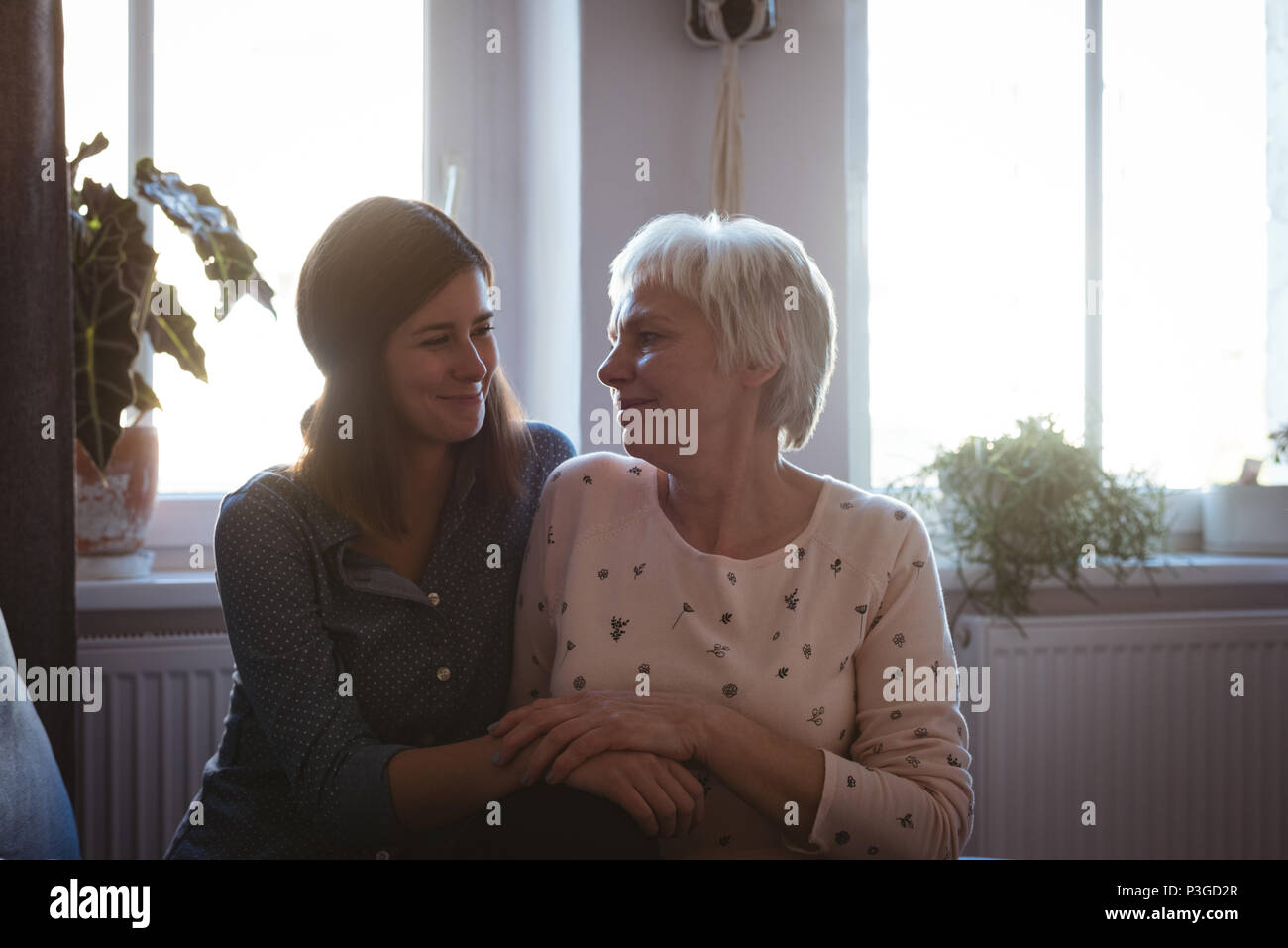 Senior woman and daughter sitting on sofa embracing each other in the living room Stock Photo