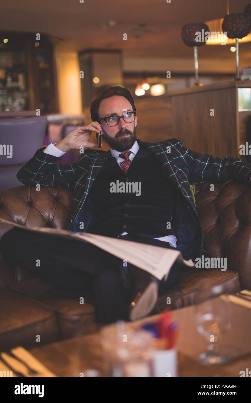 Businessman taking on mobile phone while reading newspaper Stock Photo