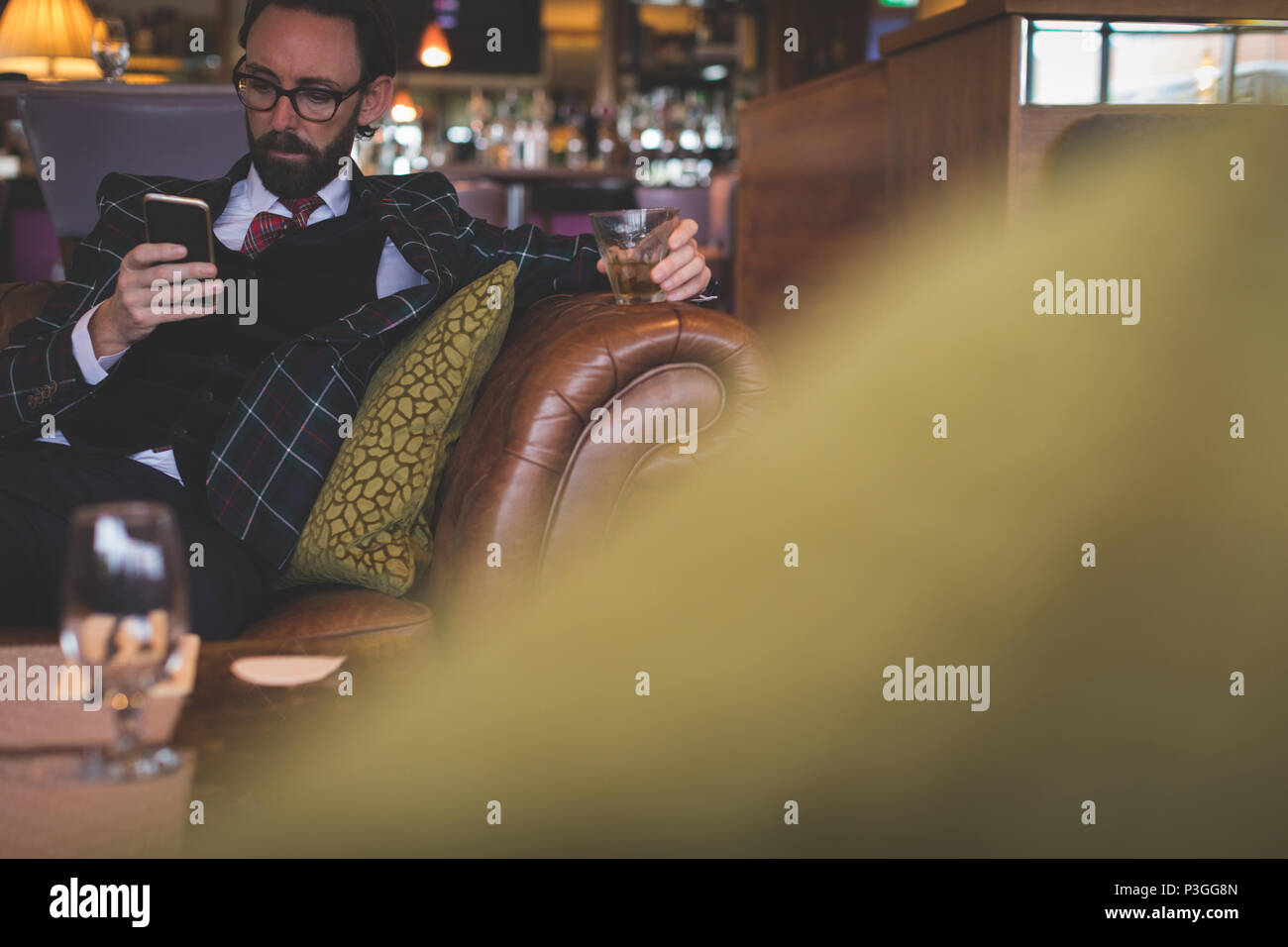 Businessman using mobile phone while having whiskey Stock Photo