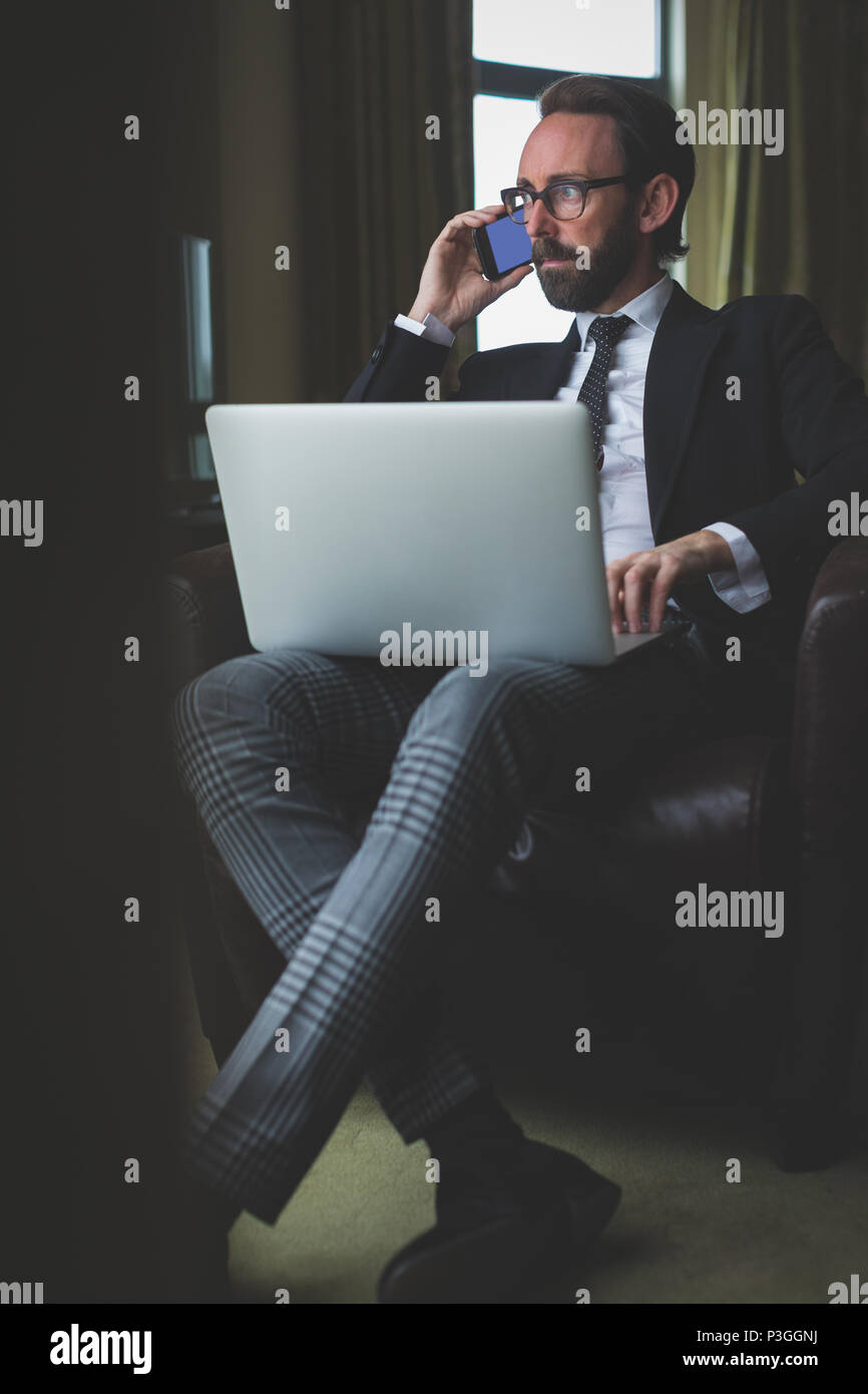 Businessman talking on mobile phone while using laptop Stock Photo