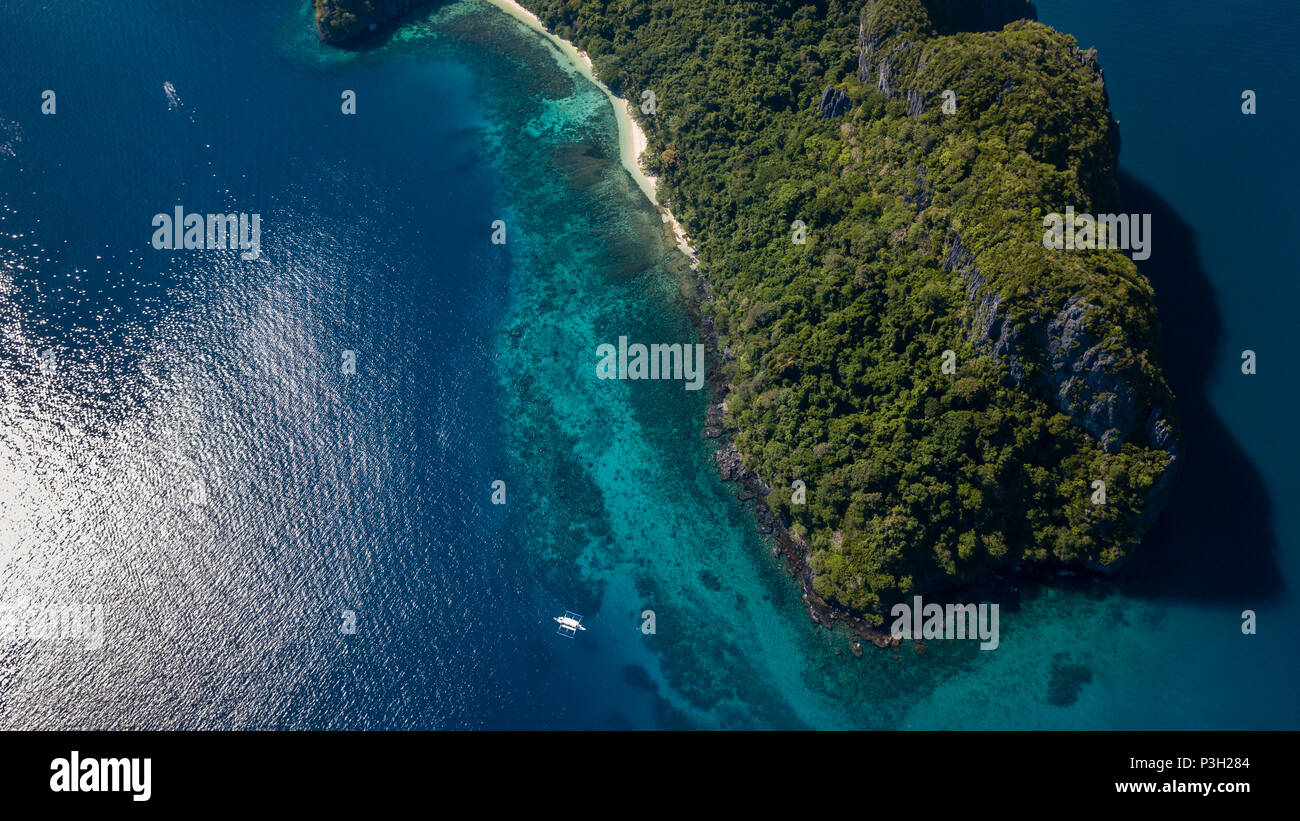 Aerial drone view of boats in a clear ocean, over a tropical coral reef, surrounded by towering jungle covered mountains Stock Photo