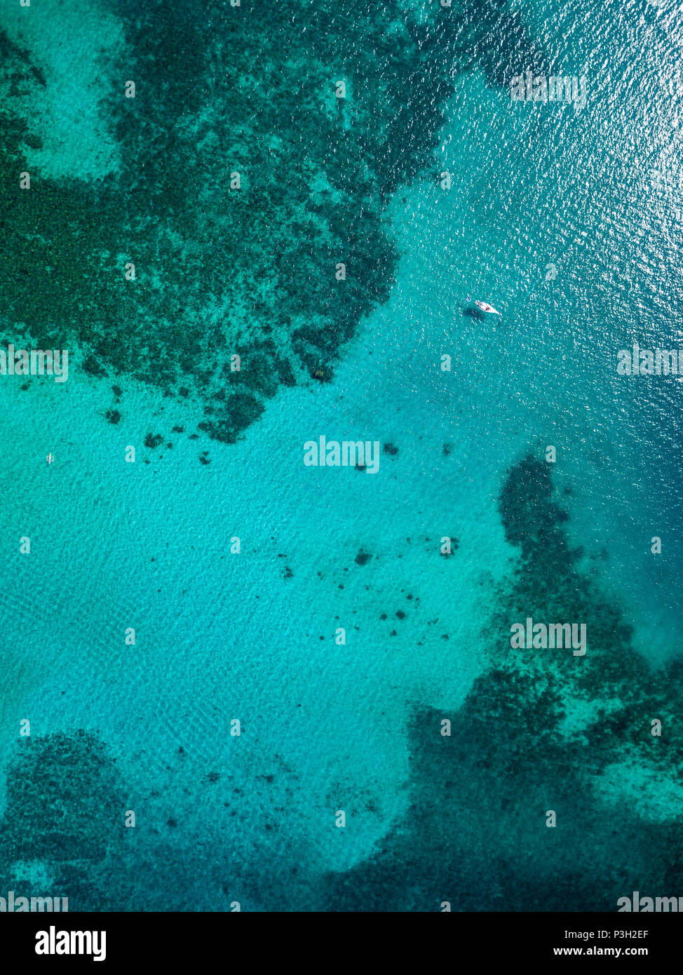 Top down aerial drown view of a small boat over a tropical coral reef in a clear ocean Stock Photo