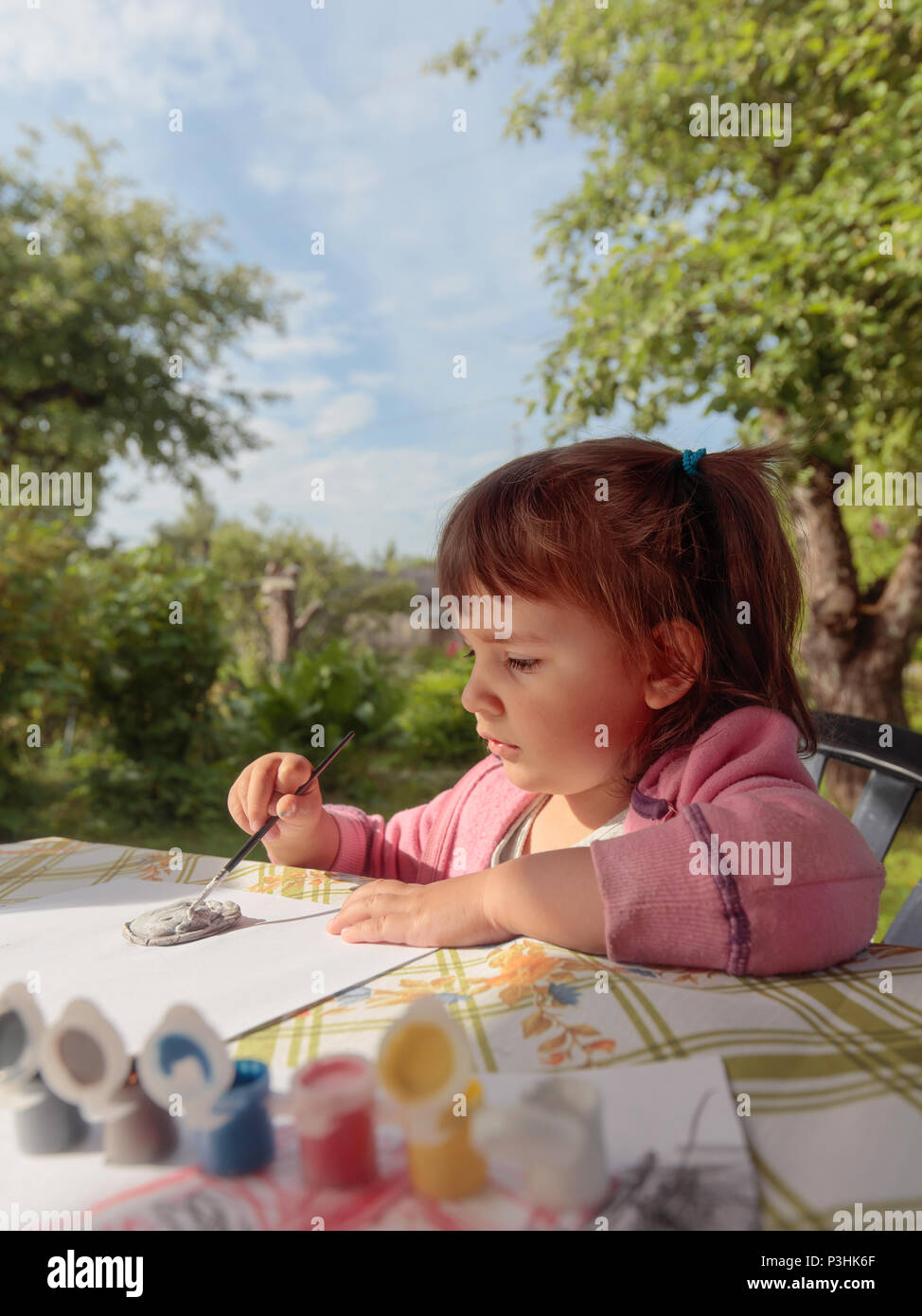 Cute little girl paints animal figures. Summer sunny day in the garden ...