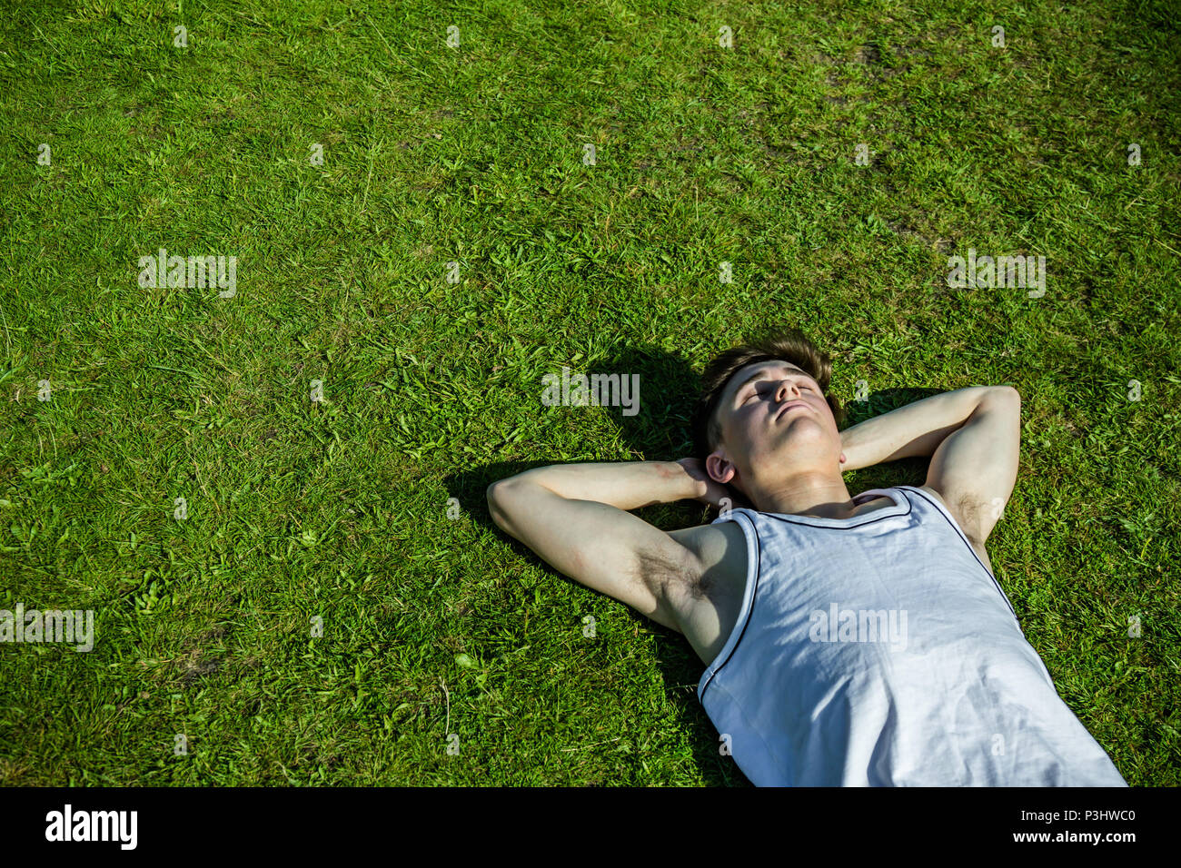 A young adult male sunbathing, laying on short grass on a warm summer's