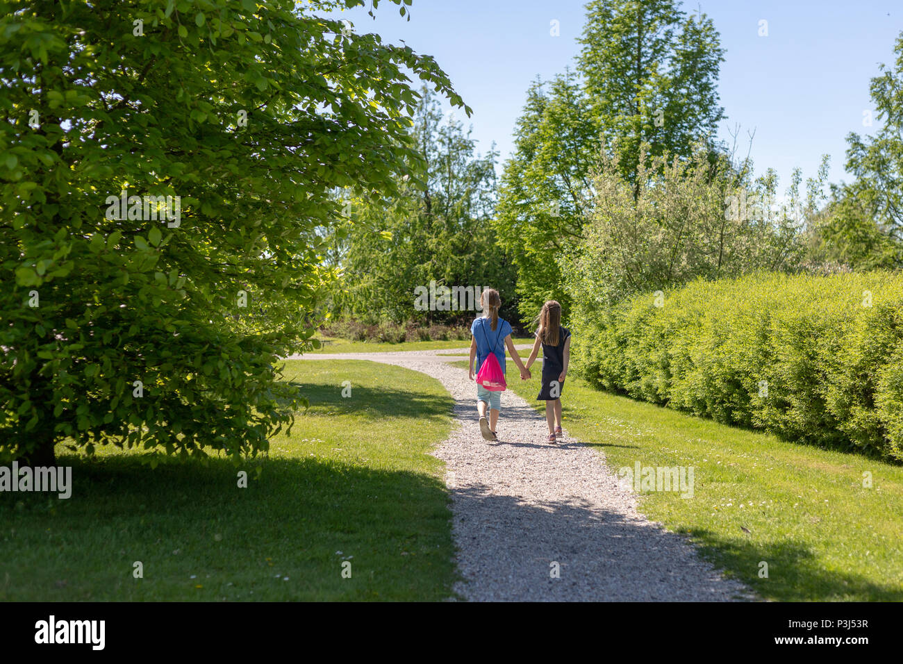 2 girls walk hand in hand on a dirt road in the park Stock Photo