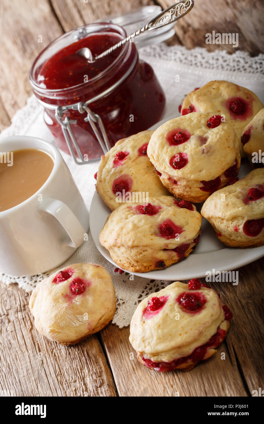 Delicious sconces biscuits with red currants are served with tea with milk and jam close-up on the table. vertical Stock Photo