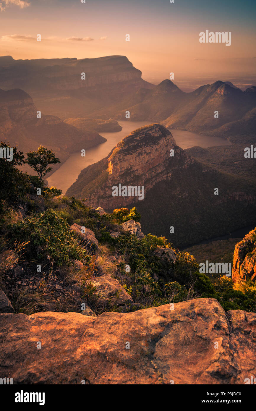 Portrait Shot of Blyde River Canyon bathed in dreamy warm pinks and oranges during pre-sunset golden hour. Foreground Rock. Mpumalanga, South Africa Stock Photo