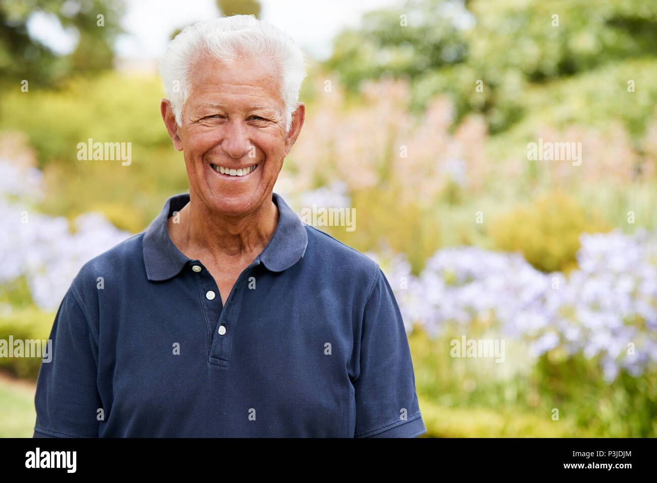 Portrait Of Senior Man Enjoying Walk By Flower Beds In Park Stock Photo