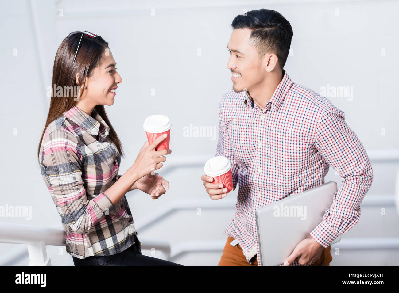 Young man and woman talking while drinking coffee during break Stock Photo