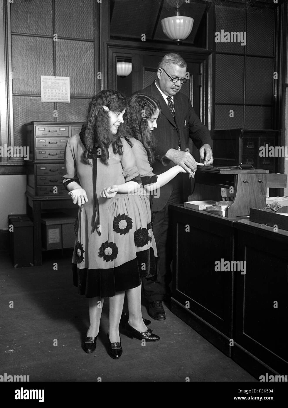 Daisy and Violet Hilton get fingerprinted. Fred Sandberg, District police fingerprint expert, tells Daisy and Violet Hilton, 'Siamese Twins,' apart by their fingerprints Stock Photo