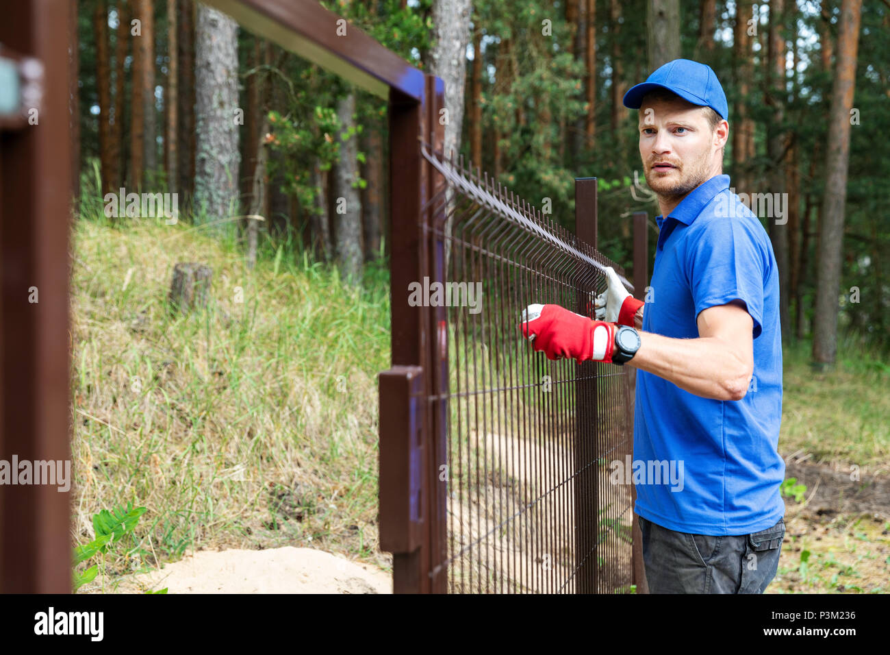 man installing brown metal fence Stock Photo