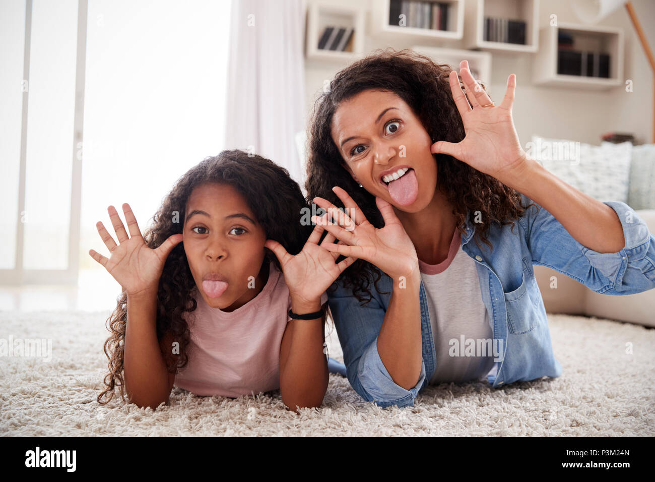 Mother And Daughter Lying On Rug And Pulling Faces At Home Stock Photo