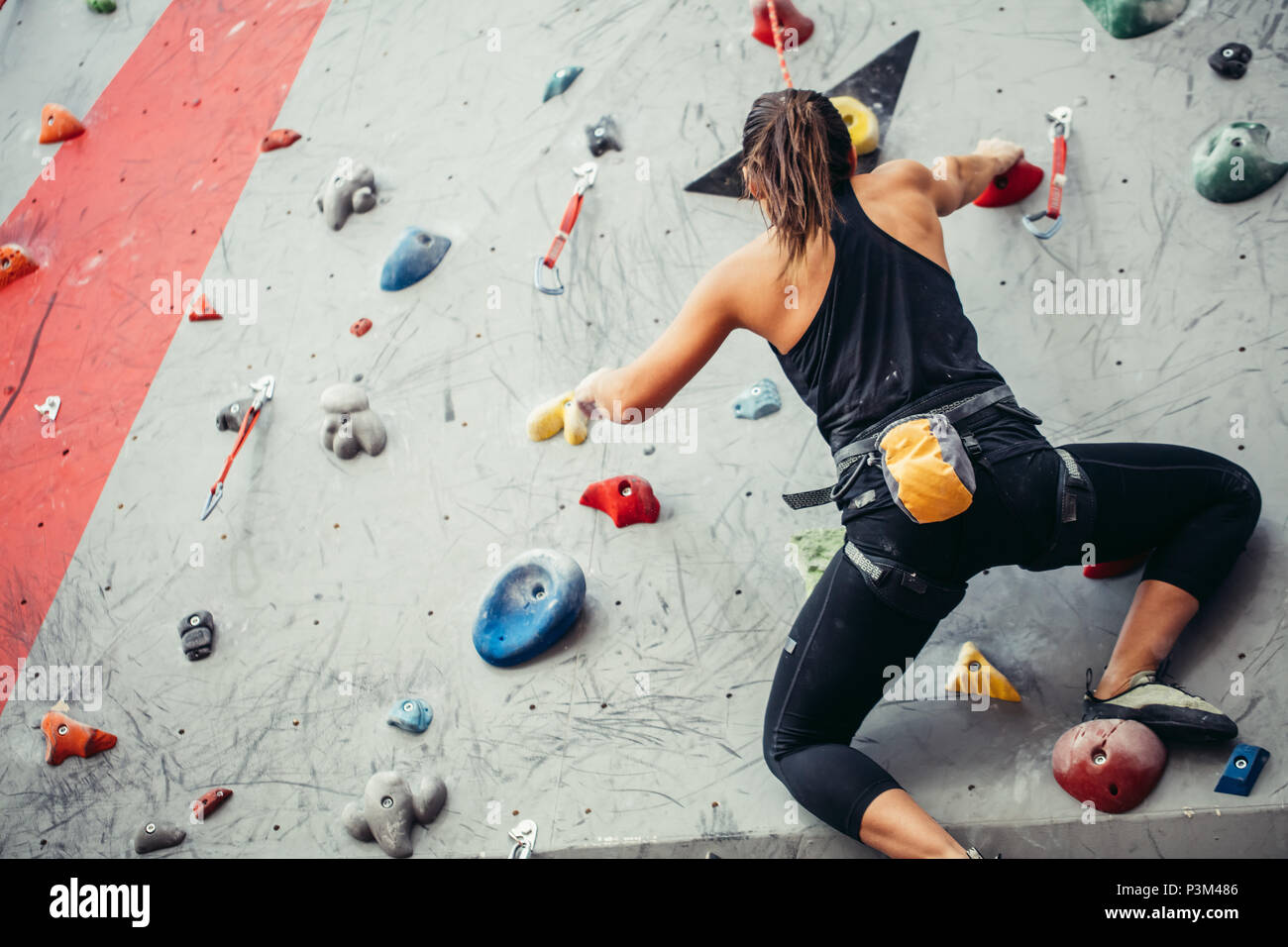 Climber young woman climbing on practical wall indoor, bouldering