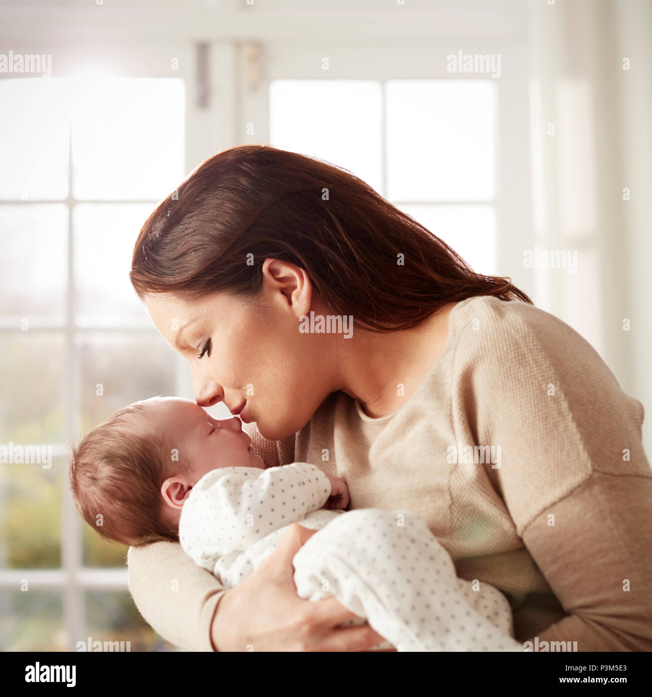 Loving Mother Kissing And Cuddling Newborn Baby At Home Stock Photo