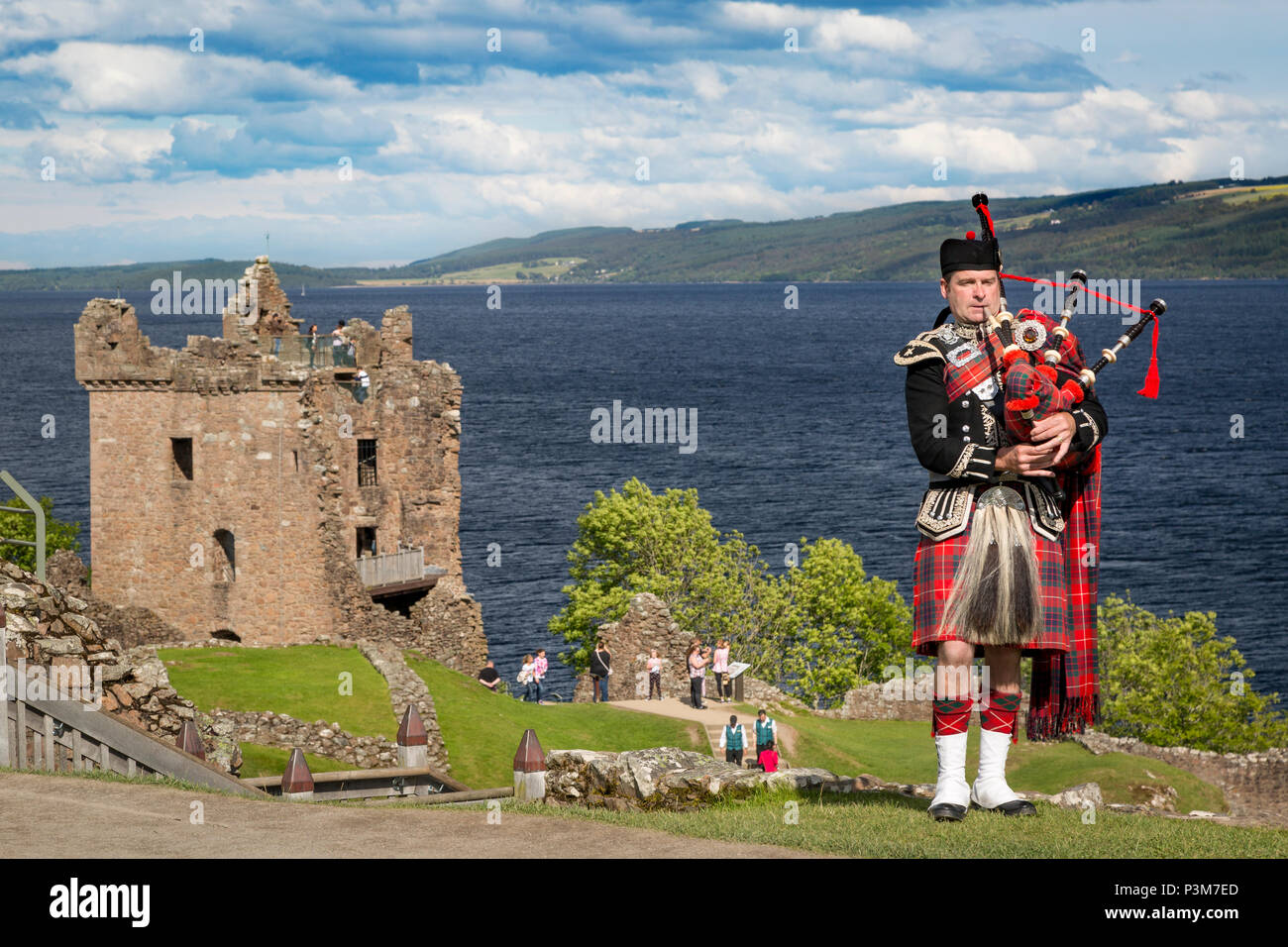 Bagpiper playing near the ruins of Urquhart Castle along the shores of Loch Ness, Highlands, Scotland, UK Stock Photo