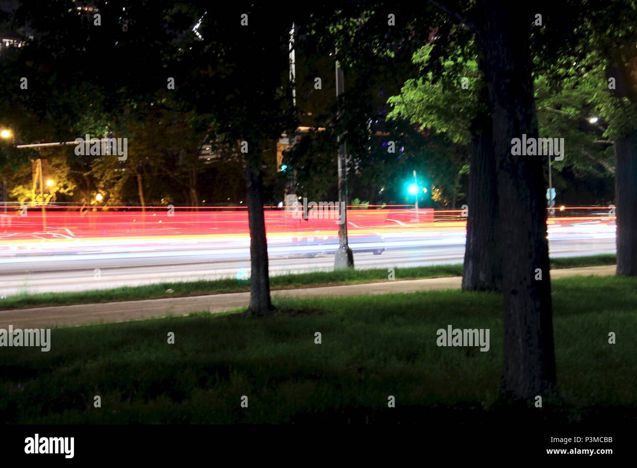 Blurred car lights between trees on a busy city street. Stock Photo