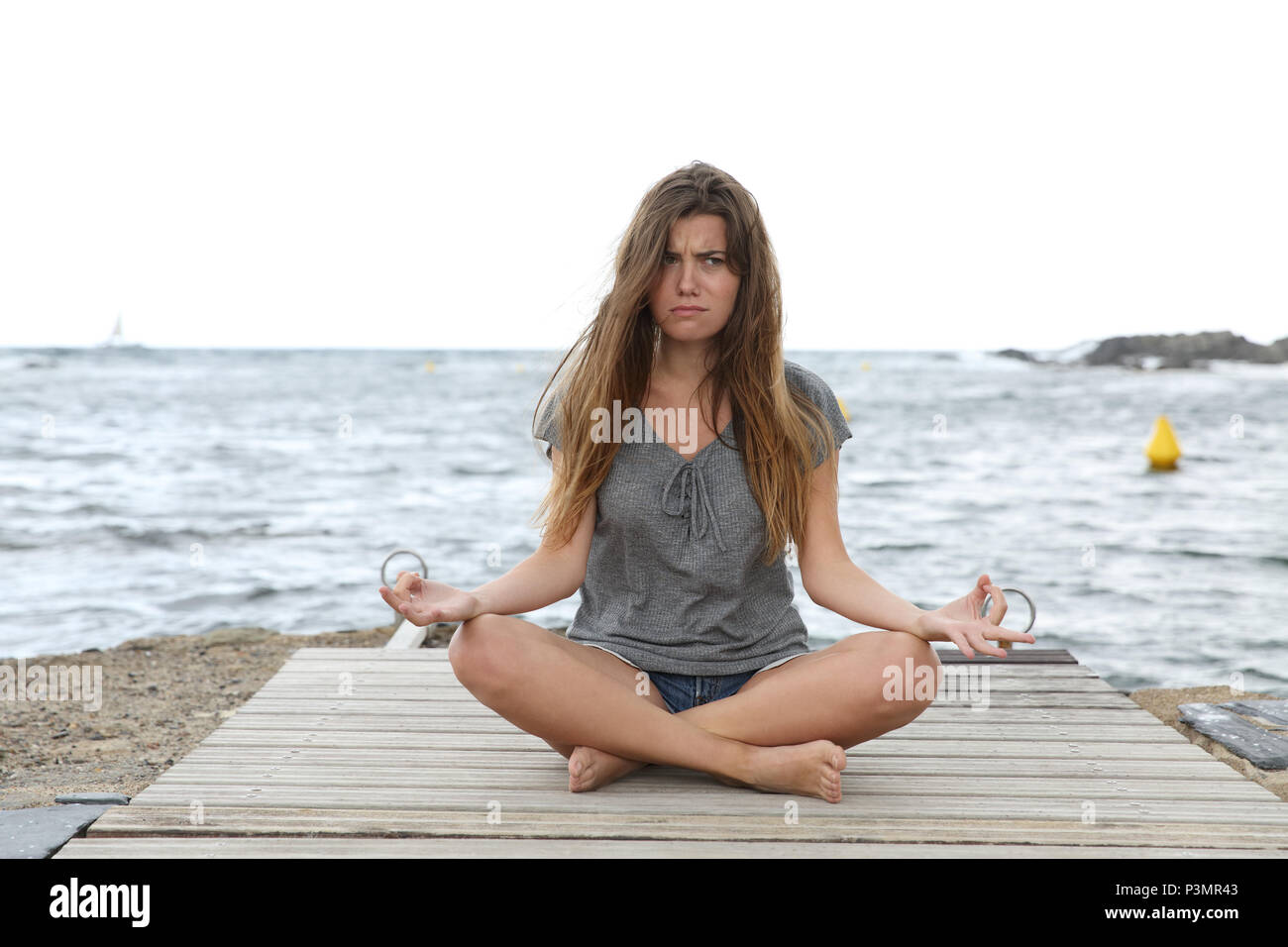 Front view full body portrait of a stressed girl trying to do yoga exercises on a pier on the beach Stock Photo