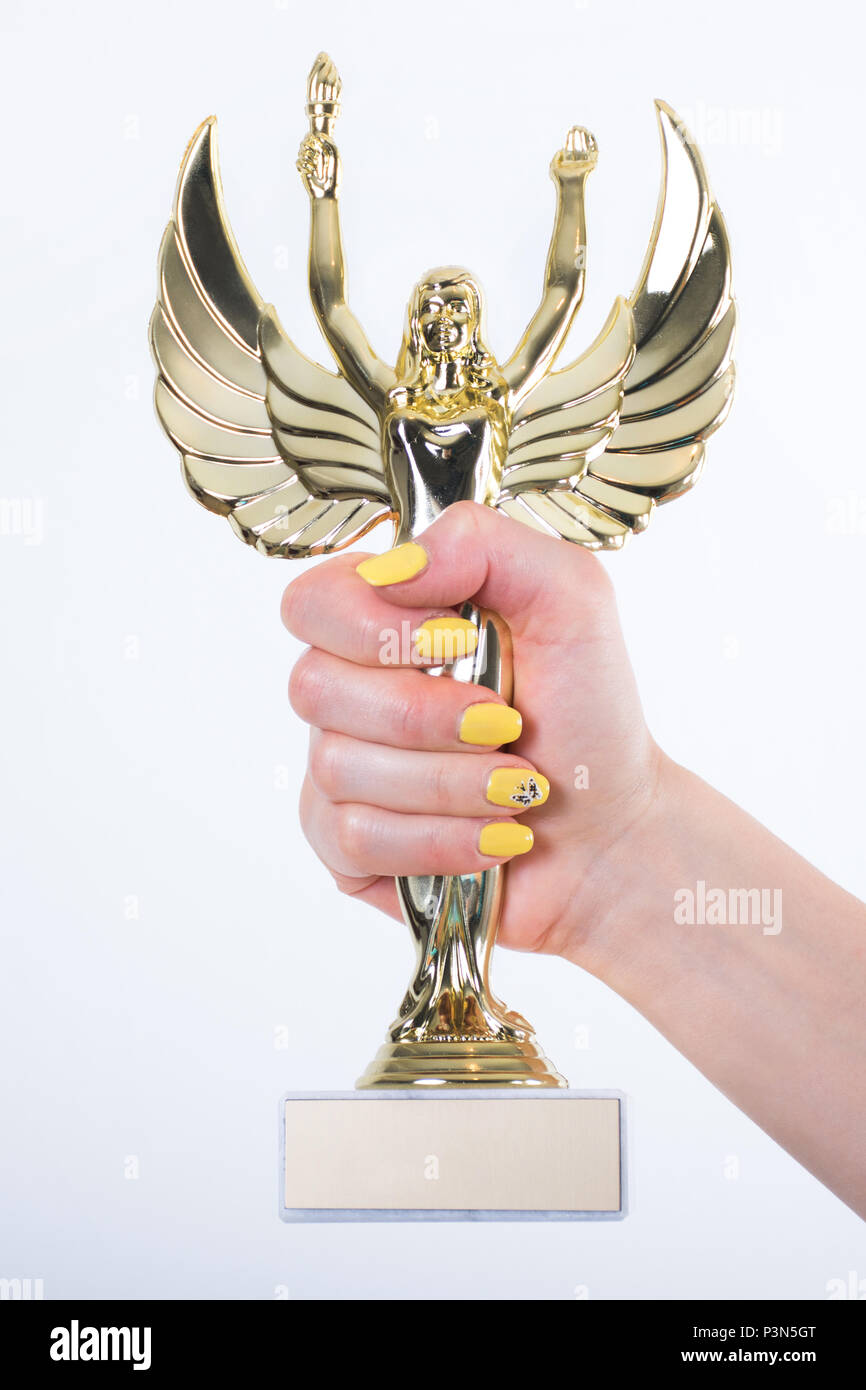Golden Angel statue with torch and opened wings in female hand with yellow manicure nails isolated on white background. Small figure with marble stand Stock Photo