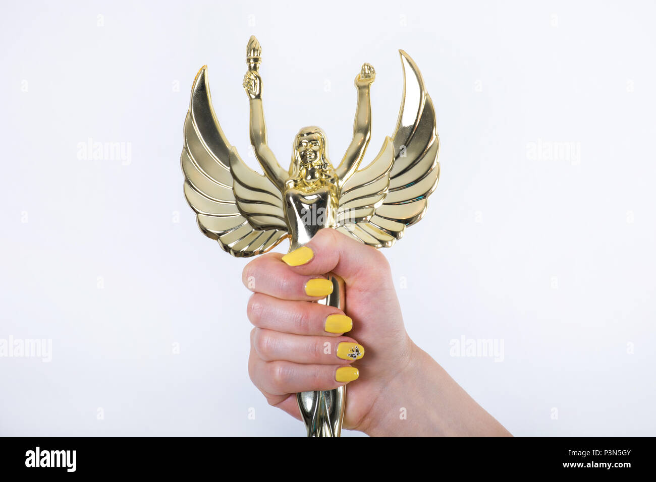 Golden Angel statue with torch and opened wings in female hand with yellow manicure nails isolated on white background. Close up, studio shoot Stock Photo