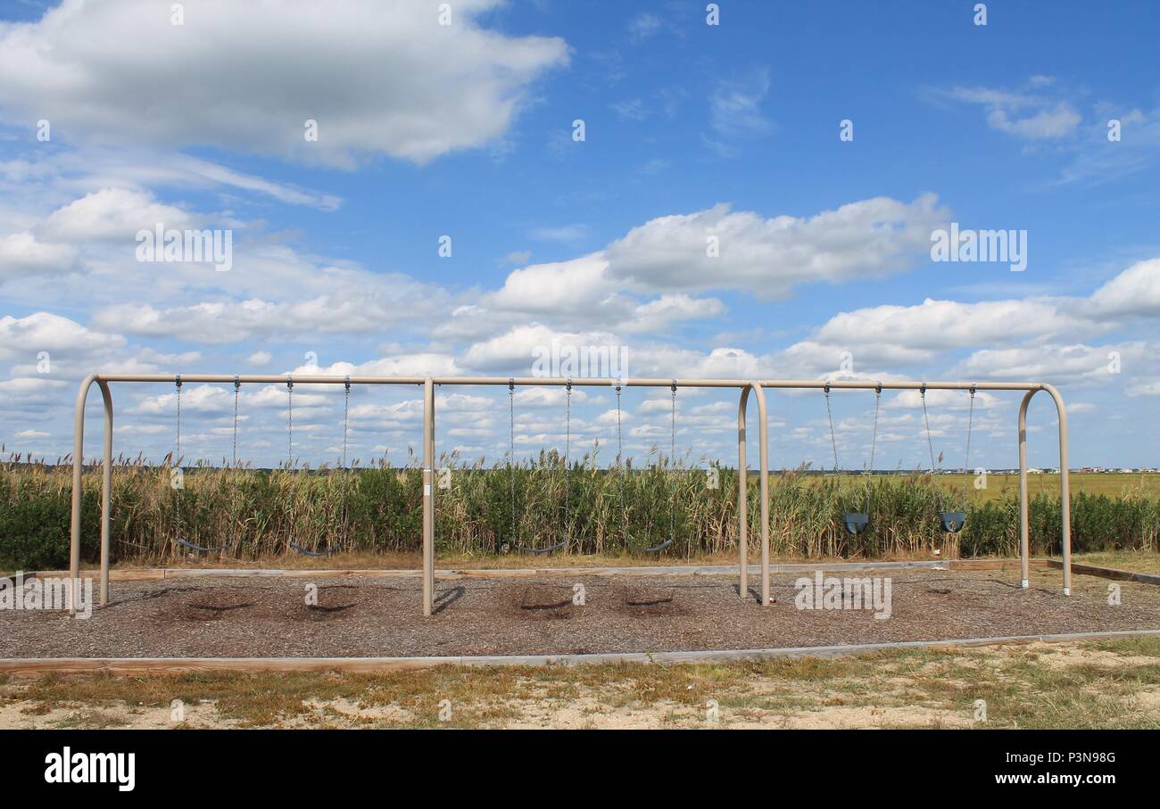 A swing set in front of smooth cordgrass under a blue sky with cumulus clouds overhead. Dock street in Little Egg Harbor Township, NJ Stock Photo