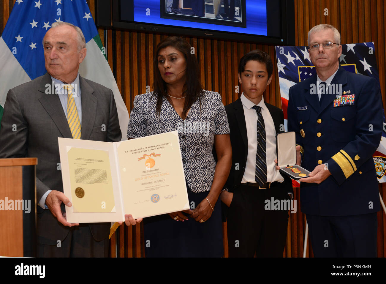 NEW YORK - Rear Adm. Steven Poulin, commander Coast Guard First District, and Hon. William Bratton, commissioner New York City Police Department, stand with Jose Rosario’s wife and son during the Gold Lifesaving Award presentation July 18, 2016, in New York City. The Coast Guard presented the award to Mr. Rosario’s family for his unselfish actions in March 2015, when he jumped in the rough waters off Puerto Rico to save the life of a child. (U.S. Coast Guard photo by Petty Officer 3rd Class Steve Strohmaier) Stock Photo