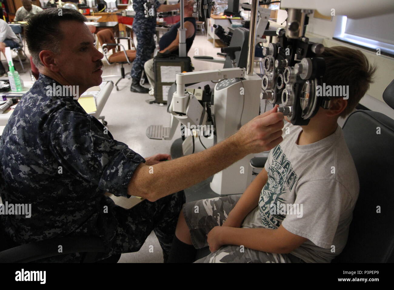 Capt. Mason Philbrook, an optometrist from the Navy Operational Support Center out of Quincy, Mass., gives a young boy an eye exam using a phoropter during the Greater Chenango Cares Innovative Readiness Training event, July 20, 2016.  Greater Chenango Cares is one of the IRT events that provides real-world training in a joint civil-military environment while delivering world-class medical care to the people of Chenango County, N.Y., from July 15-24. Stock Photo
