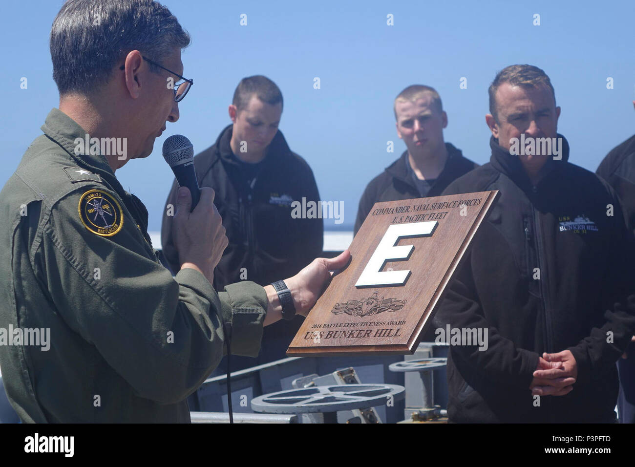 PACIFIC OCEAN (May 10, 2017) Rear Adm. Jay Bynum presents the 2016 Battle Effectiveness Award, Battle 'E,' to Capt. Joe Cahill, commanding officer of the guided-missile cruiser USS Bunker Hill (CG 52). Bunker Hill is underway participating in a group sail training unit exercise with the Theodore Roosevelt Carrier Strike Group. Group sail is the first step in Bunker Hill’s integrated training phase and aims to enhance mission-readiness and warfighting capabilities between the ships, air wings and the staffs through simulated real-world scenarios. Stock Photo