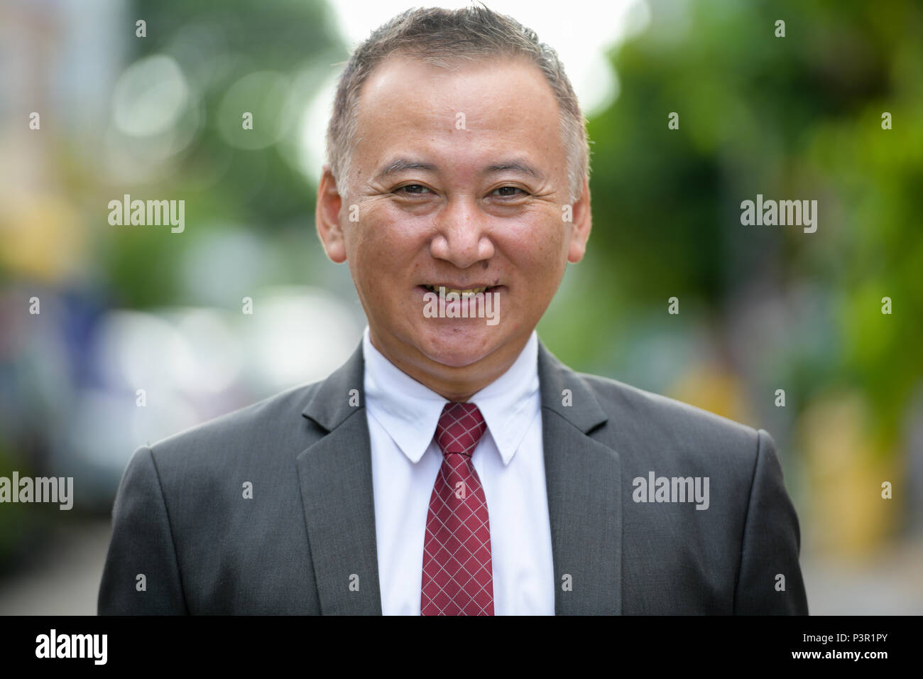 Mature happy Japanese businessman smiling in the streets outdoors Stock