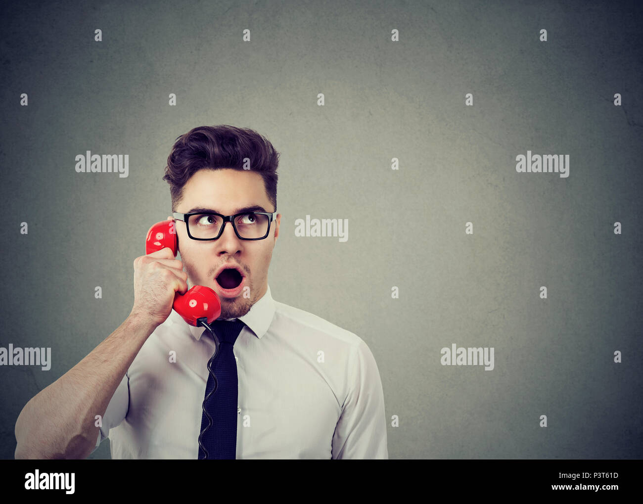 Amazed shocked young business man talking on a red telephone Stock Photo