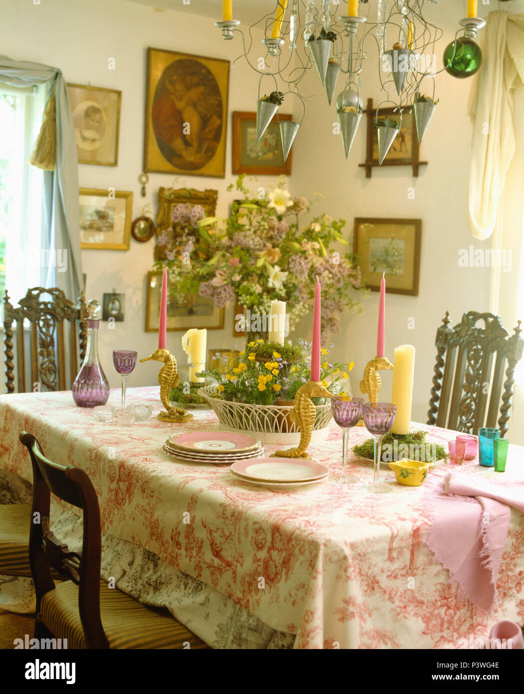 Pink+white cloth on table with pink candles and vase of summer flowers in cottage dining room with metal chandelier Stock Photo