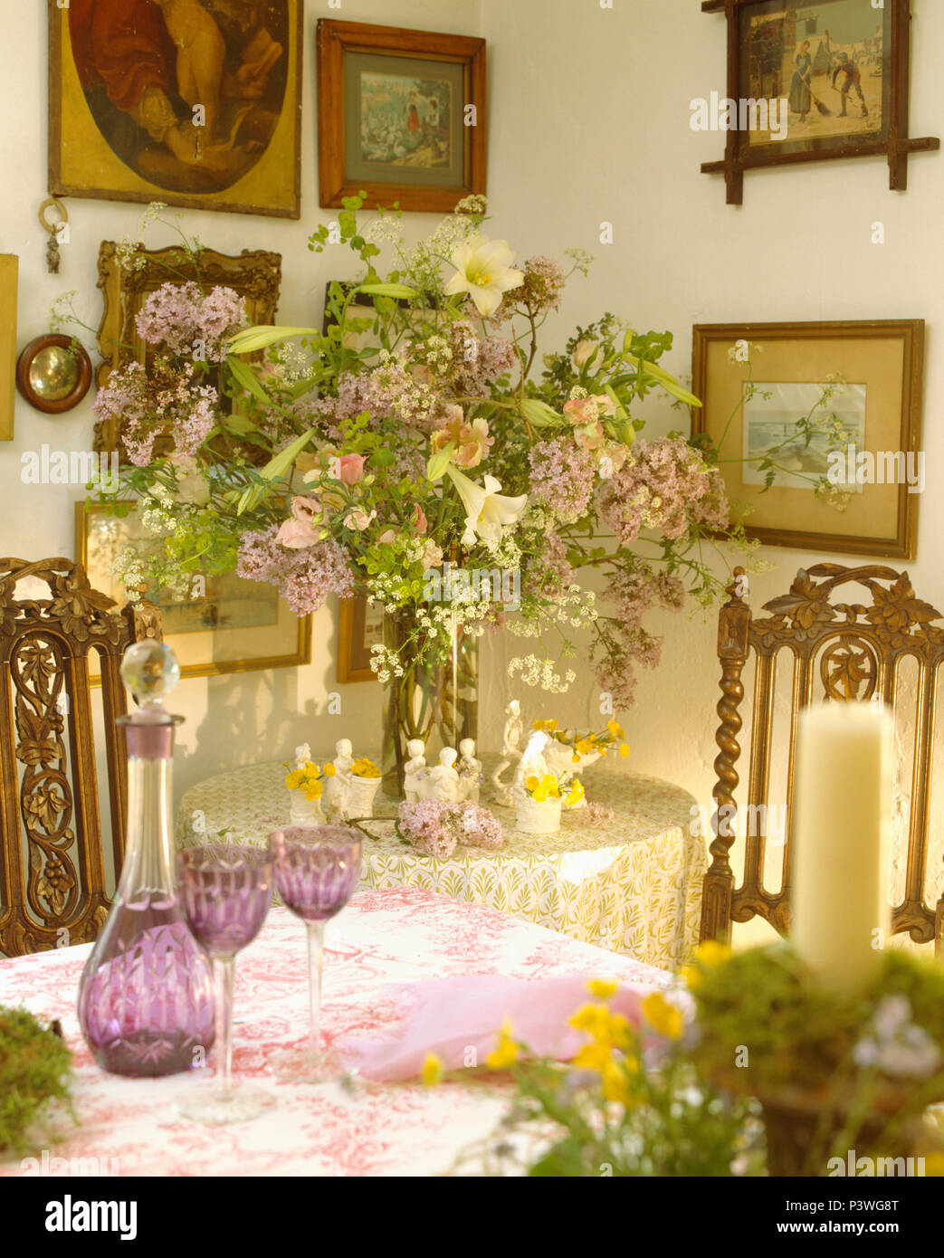 Pictures above vase of summer flowers on corner table in cottage dining room with amethyst glasses and decanter Stock Photo