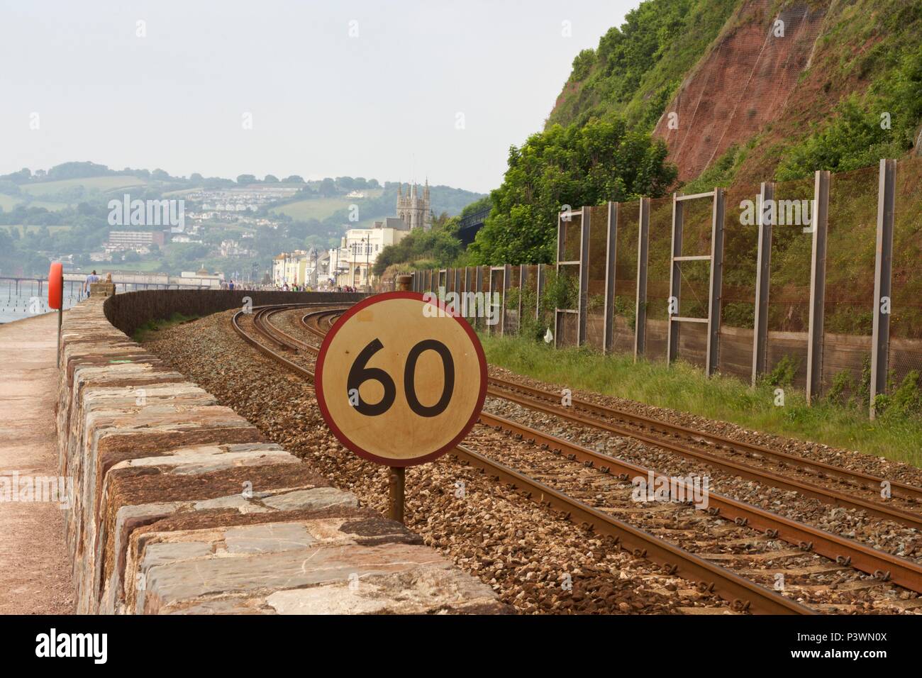 A 60mph train limit sign along empty railway train tracks on the Riviera line running along the sea wall in Teignmouth, South Devon Stock Photo