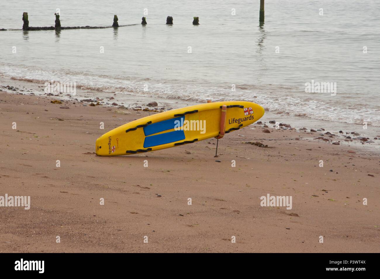 A RNLI lifeguard surf board propped up on the beach at Teignmouth, South Devon Stock Photo