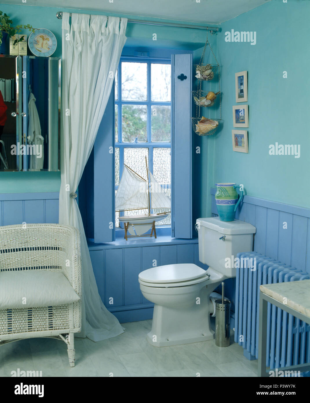 wcker-chair-beside-white-curtains-on-window-with-painted-shutters-in-blue-bathroom-with-tonguegroove-paneling-P3WY7K.jpg