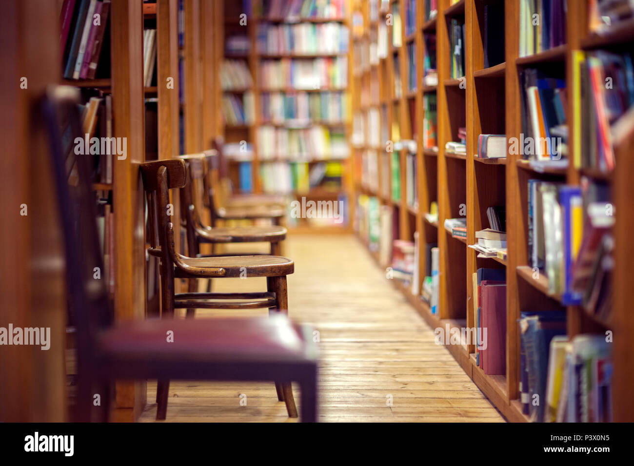 Library with rows of books on shelves and empty chairs Stock Photo