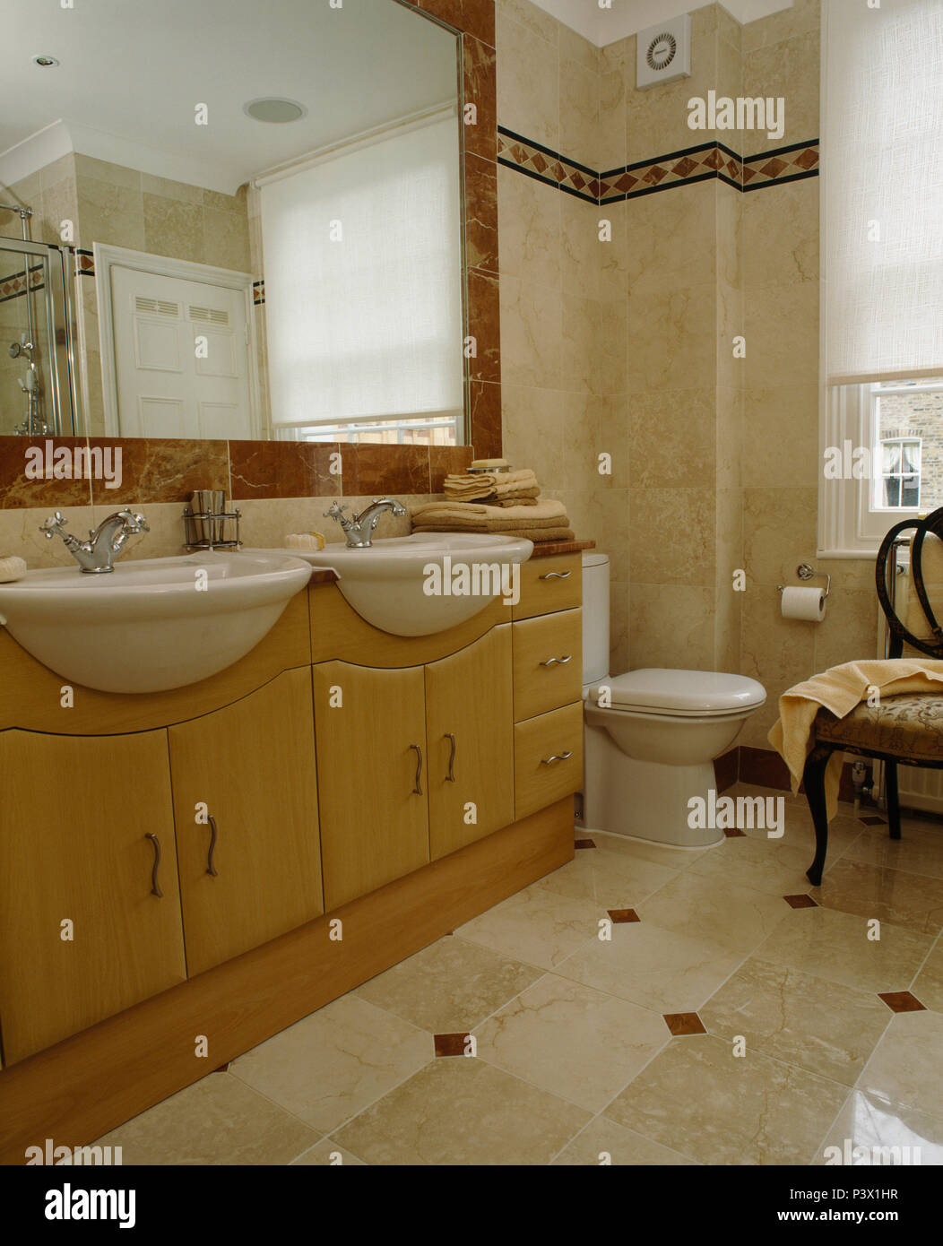 Large mirror above pale wood vanity unit with double basins in marble