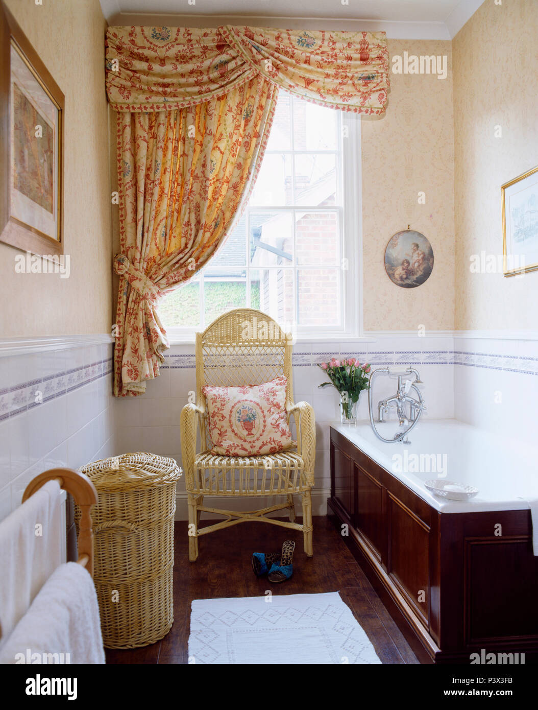 Red Patterned Swagged Pelmet And Curtain On Window In Narrow Bathroom With Wicker Laundry Basket And Armchair Stock Photo Alamy