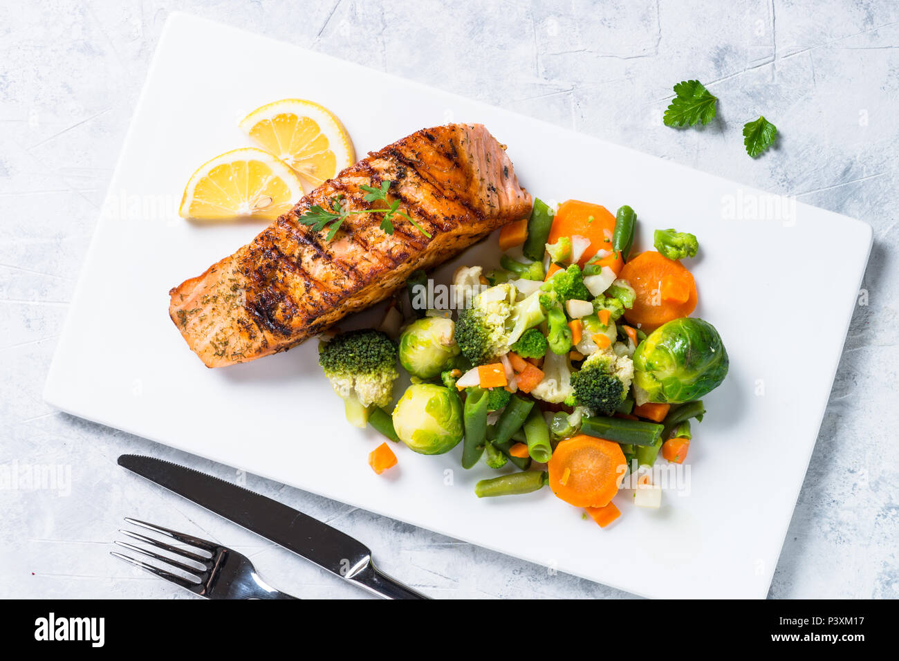 Grilled salmon fish fillet with vegetables mix on white plate. Top view ...