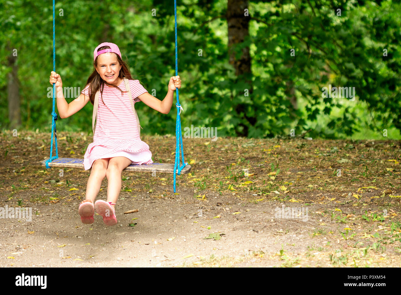 Little girl swinging on a sunny day with trees in the background Stock Photo
