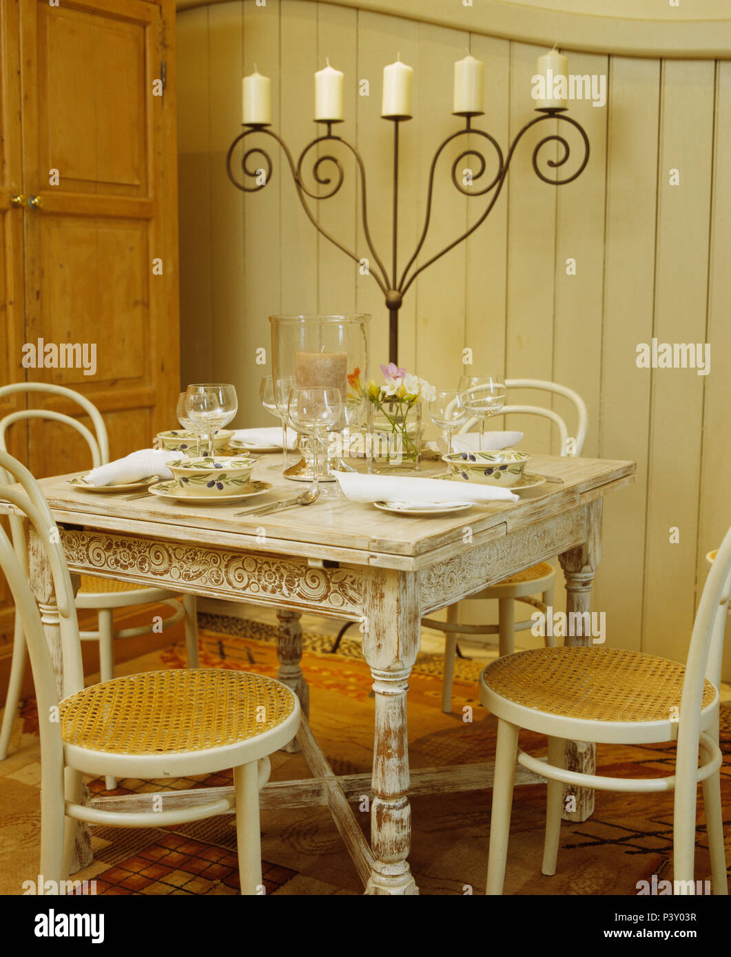 Bentwood chairs at lime-washed table set for lunch with tall wrought iron candelabra in dining room in stable conversion Stock Photo