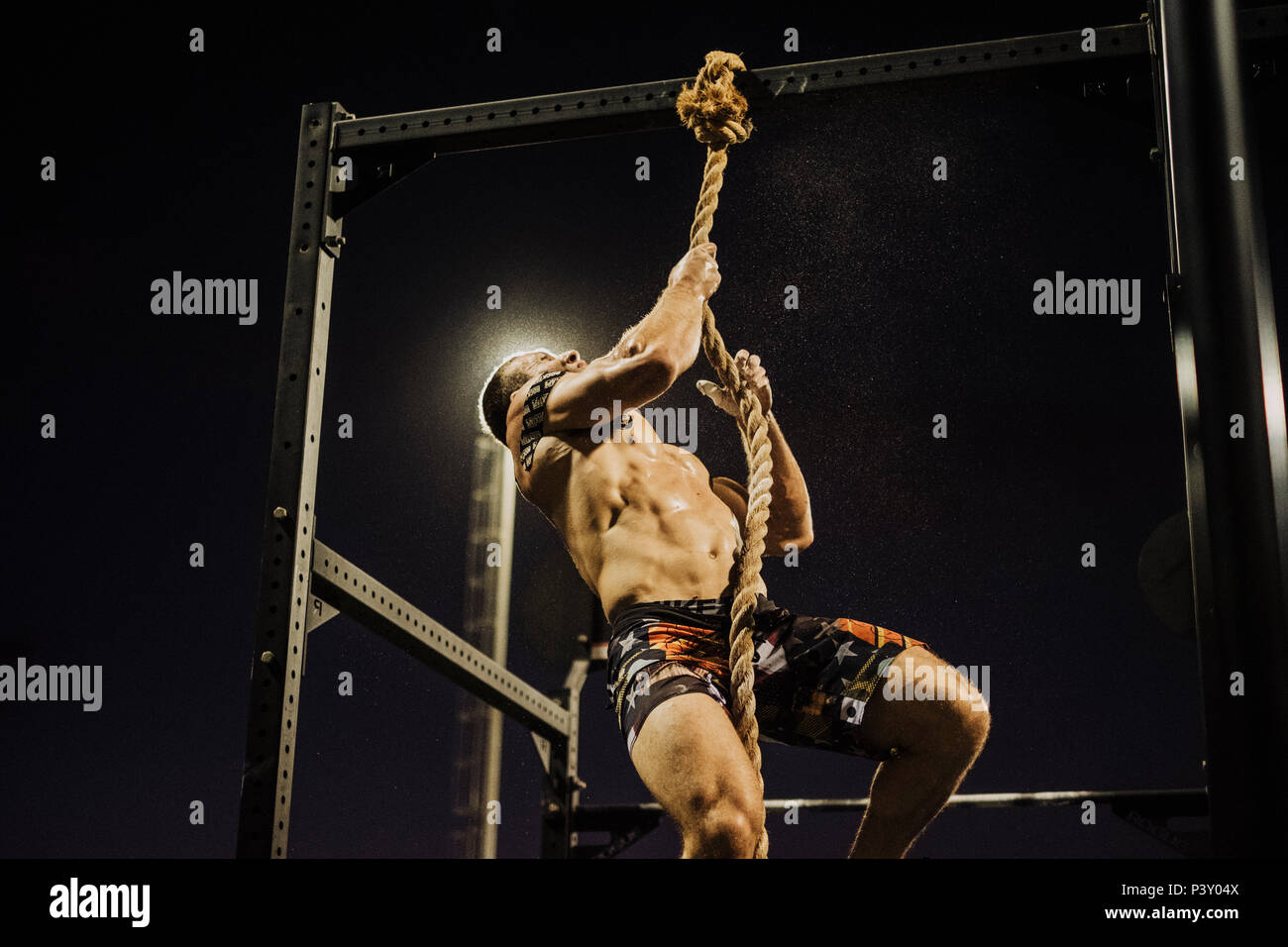 a night time shoot of a crossfit athlete climbing up a rope Stock Photo