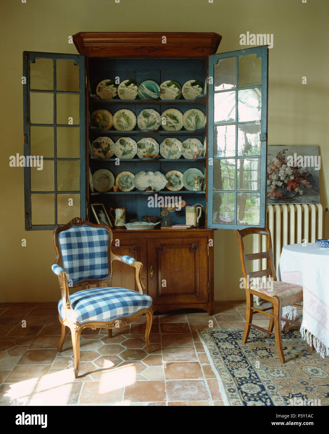 Blue+white checked upholstered Louis chair in front of antique glass front dresser in French dining room Stock Photo