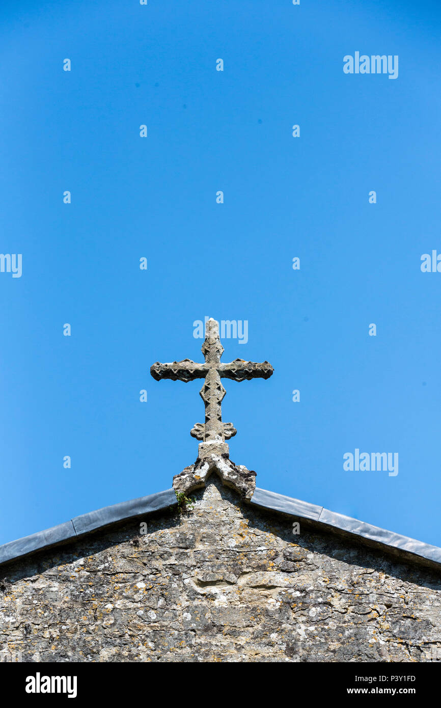 An old stone cross on the oof of a church set against a deep blue sky ...