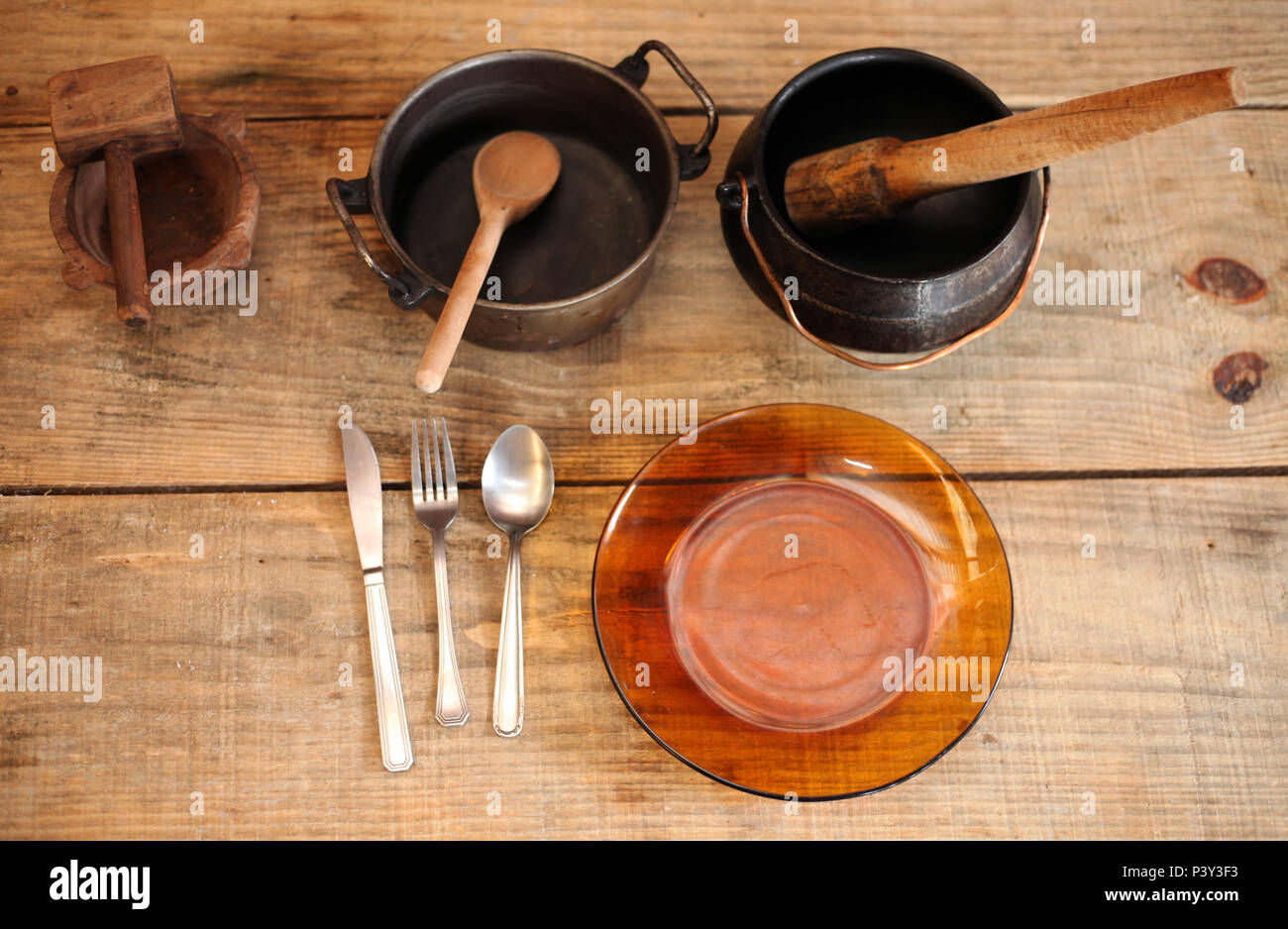 Panela de ferro com colher de madeira, panela de ferro, com amassador de  feijão em madeira, faca, garfo e colher em metal e prato de vidro escuro em  cima de mesa de