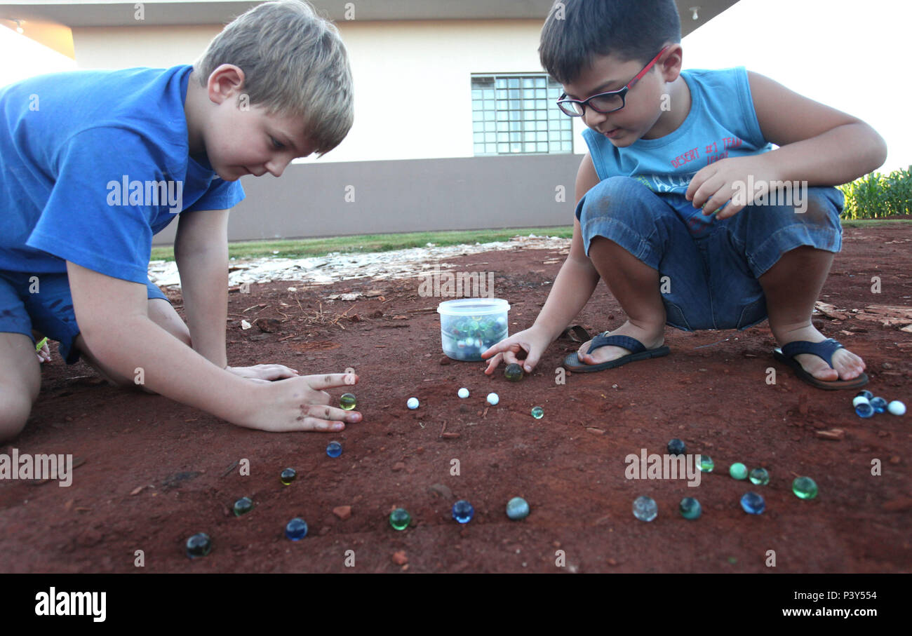 Apesar de toda a tecnologia disponível e de fácil acesso em Campo Mourão, na Região Centro-Oeste do Paraná, o jogo de bolinha de gude ainda fascina crianças do interior. Na foto, os estudantes Guilherme e Vitor disputam uma partida de bolinha de gude em um triângulo desenhado na terra, na casa dos avós de Guilherme. Stock Photo