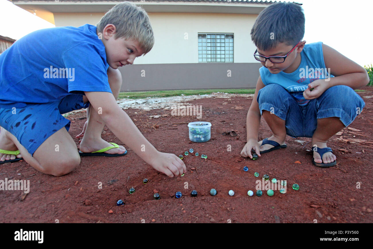 Apesar de toda a tecnologia disponível e de fácil acesso em Campo Mourão, na Região Centro-Oeste do Paraná, o jogo de bolinha de gude ainda fascina crianças do interior. Na foto, os estudantes Guilherme e Vitor disputam uma partida de bolinha de gude em um triângulo desenhado na terra, na casa dos avós de Guilherme. Stock Photo