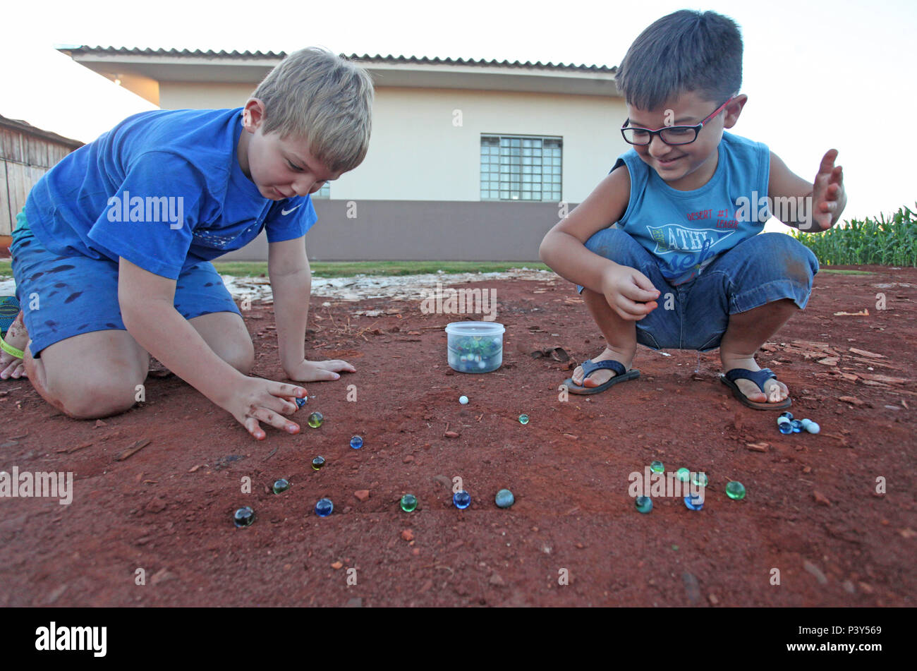 Apesar de toda a tecnologia disponível e de fácil acesso em Campo Mourão, na Região Centro-Oeste do Paraná, o jogo de bolinha de gude ainda fascina crianças do interior. Na foto, os estudantes Guilherme e Vitor disputam uma partida de bolinha de gude em um triângulo desenhado na terra, na casa dos avós de Guilherme. Stock Photo