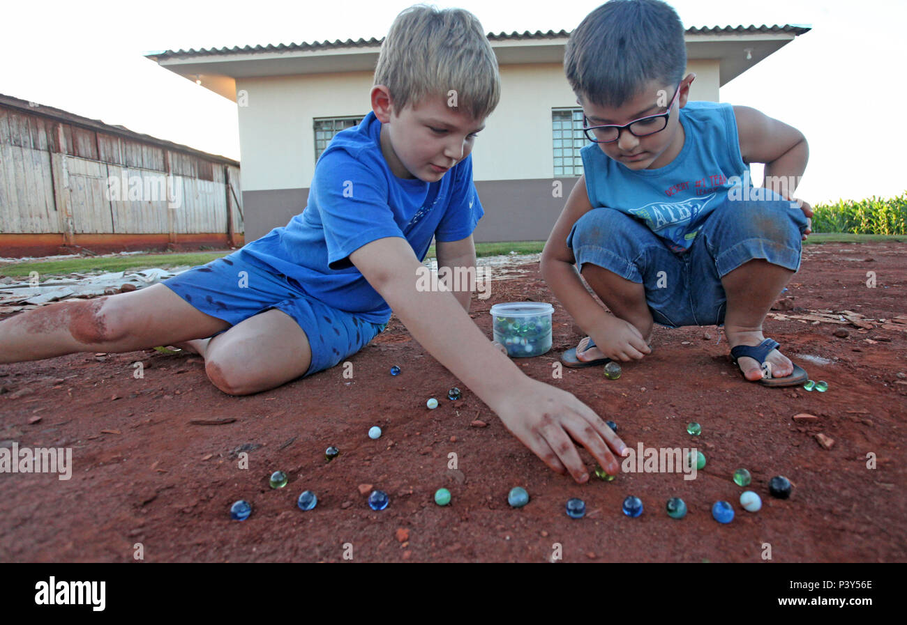 Apesar de toda a tecnologia disponível e de fácil acesso em Campo Mourão, na Região Centro-Oeste do Paraná, o jogo de bolinha de gude ainda fascina crianças do interior. Na foto, os estudantes Guilherme e Vitor disputam uma partida de bolinha de gude em um triângulo desenhado na terra, na casa dos avós de Guilherme. Stock Photo